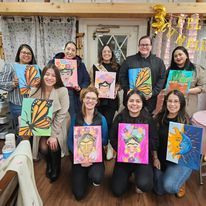 A group of people are posing for a picture while holding paintings.