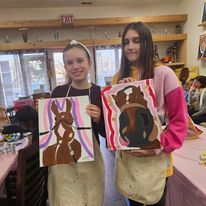 Two young women are holding paintings of horses in a room.