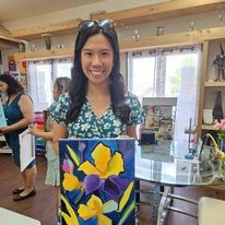 A woman is holding a painting of flowers in a room.