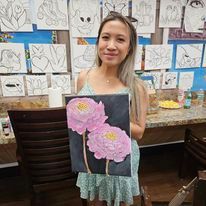 A woman is holding a painting of two pink flowers on a black background.