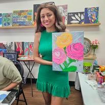 A woman in a green dress is holding a painting of flowers.