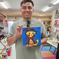 A man is holding a painting of a pikachu in a witch costume.