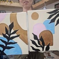 A woman is holding two paintings of leaves on canvas.
