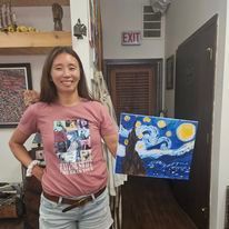 A woman is standing in a hallway holding a painting of a starry night.
