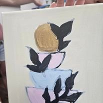 A person is holding a painting of a stack of cups with leaves on them.