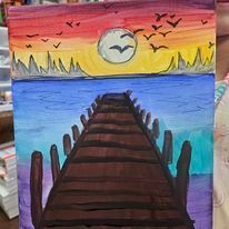 A person is holding a painting of a pier at sunset.