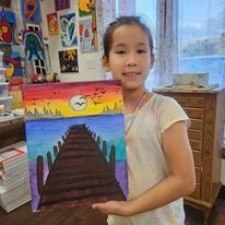 A young girl is holding a painting of a bridge over a body of water.