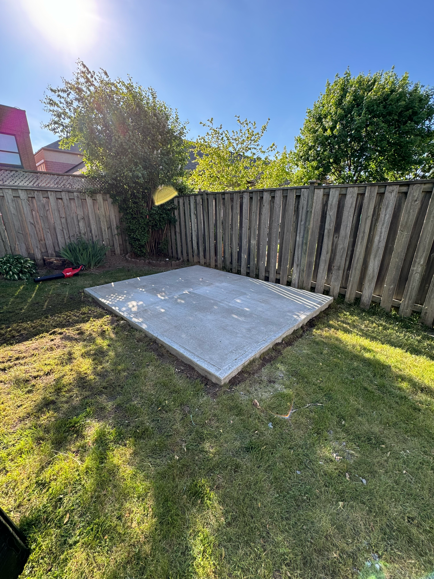 A concrete slab is sitting in the middle of a grassy yard next to a wooden fence.