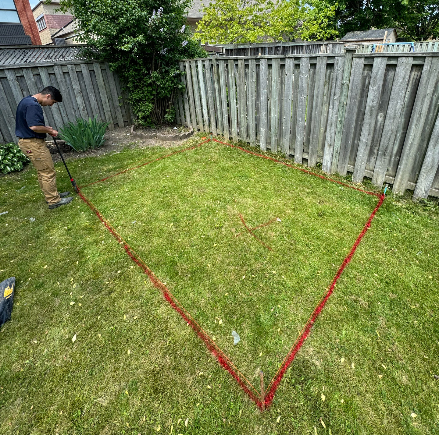 A man is measuring a triangle in the grass in a backyard.