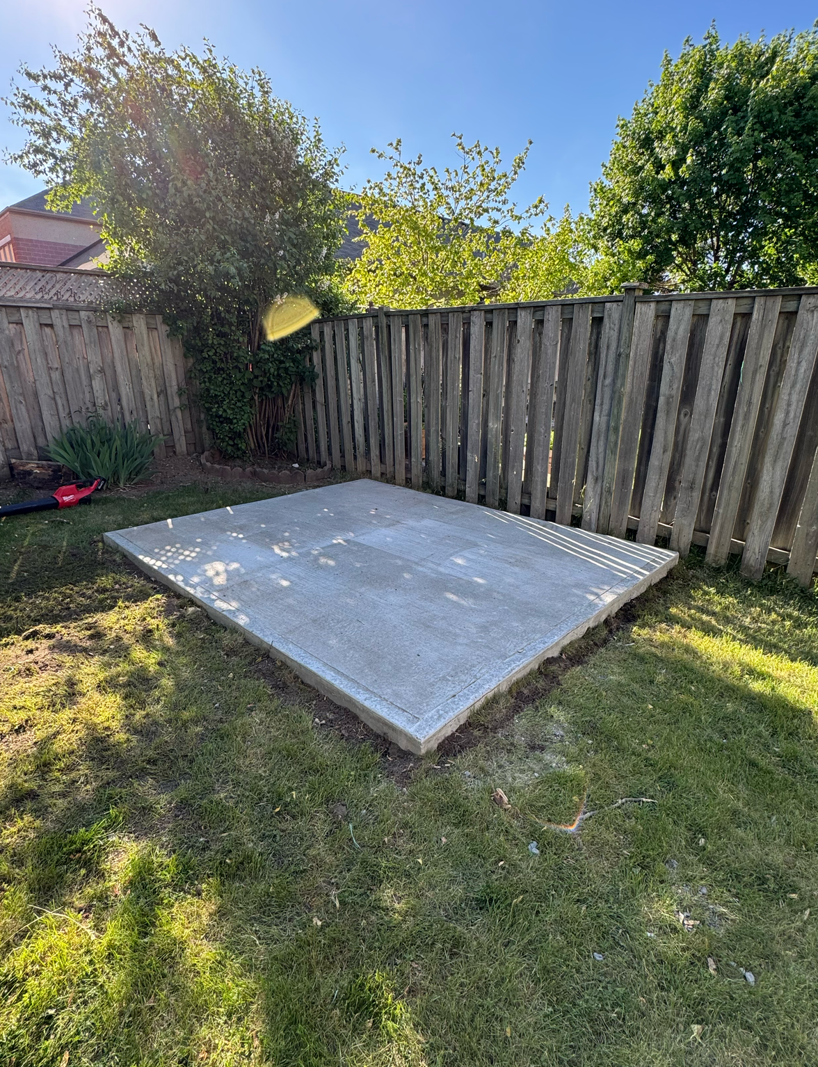 A concrete slab is sitting in the middle of a grassy yard next to a wooden fence.