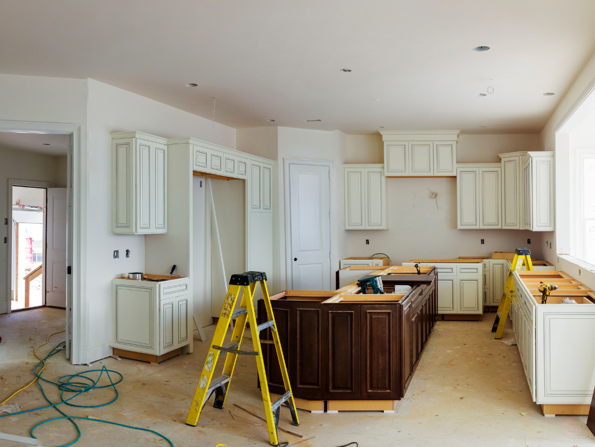 Kitchen under renovation with white cabinets, island, ladders, and tools on the floor
