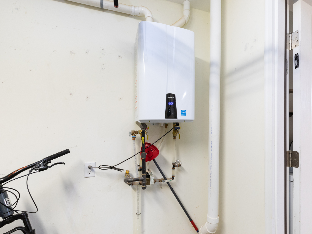 Wall-mounted water heater with pipes and a red tool in a garage-like utility area