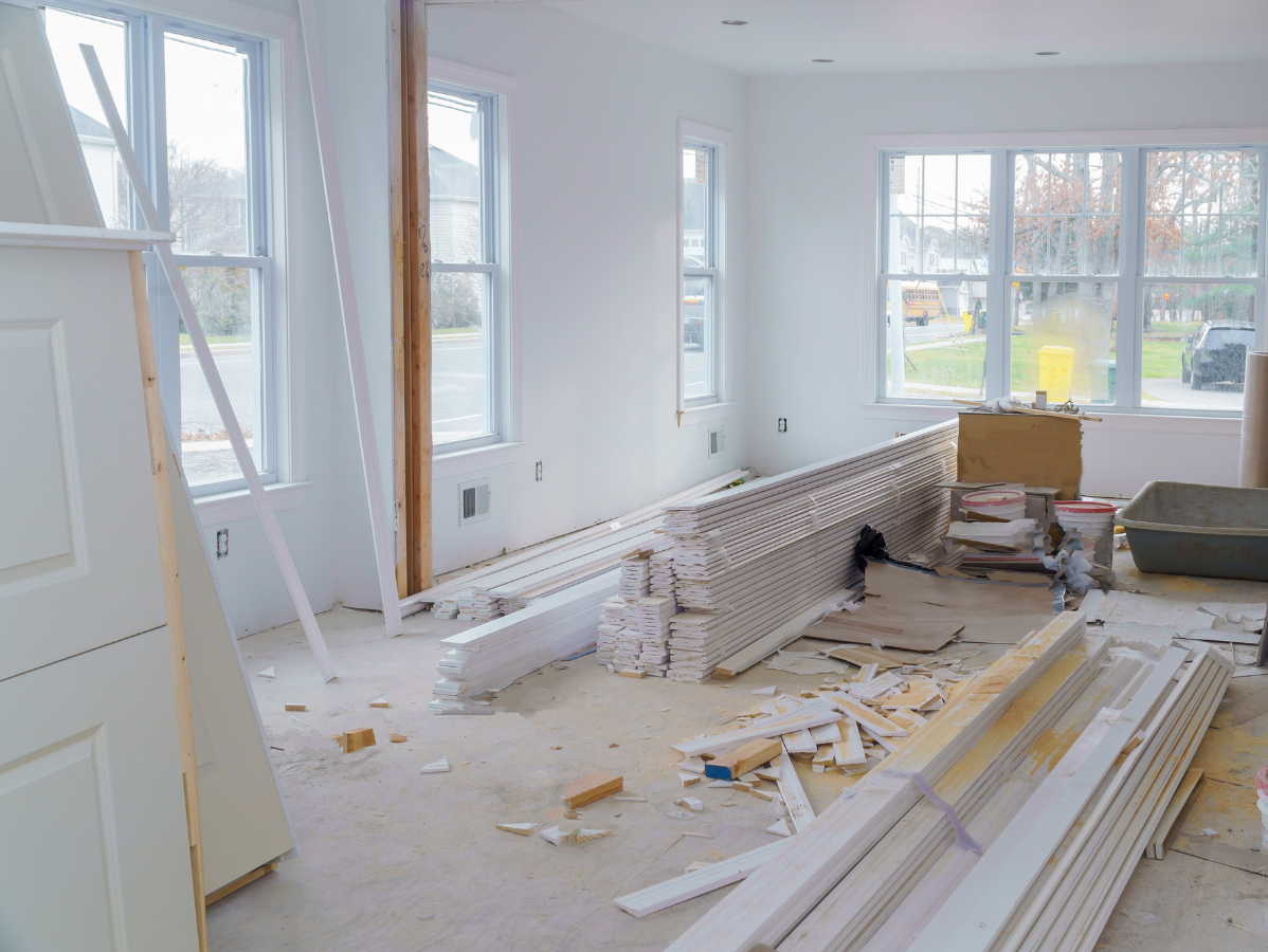 Room under renovation with scattered wood, ladders, and debris by large windows
