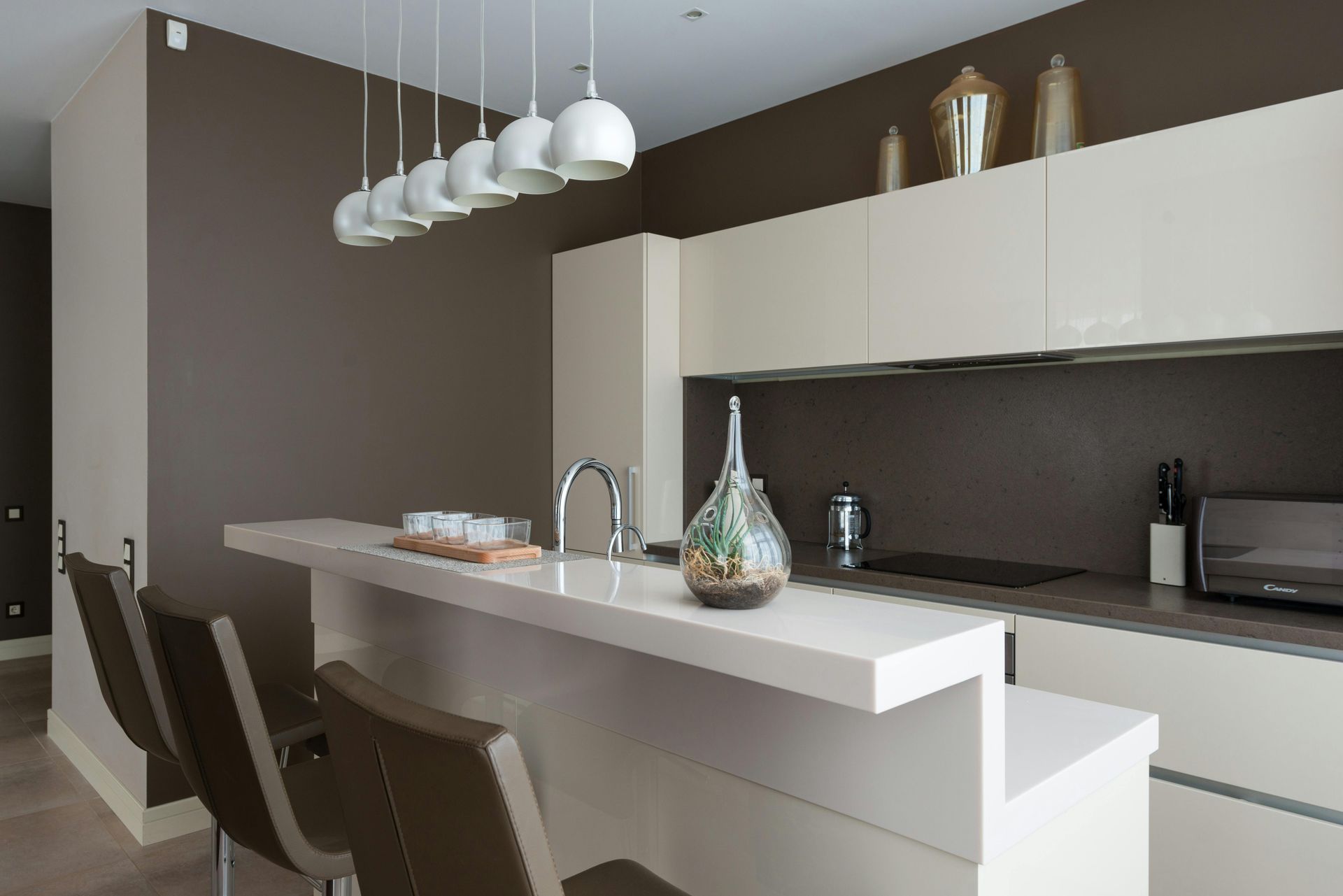 Modern kitchen with a white countertop and bar stools, brown wall and cabinets.