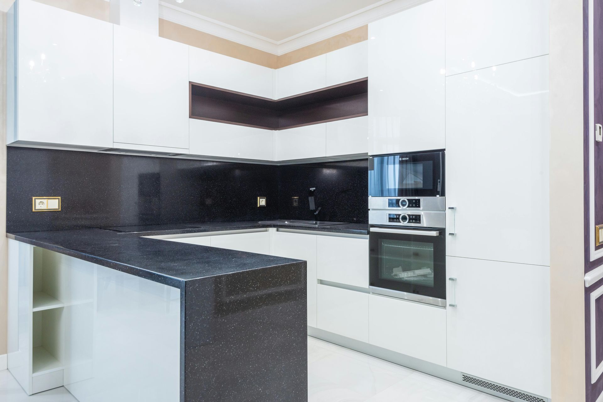 Modern white kitchen with black speckled countertops and built-in appliances.