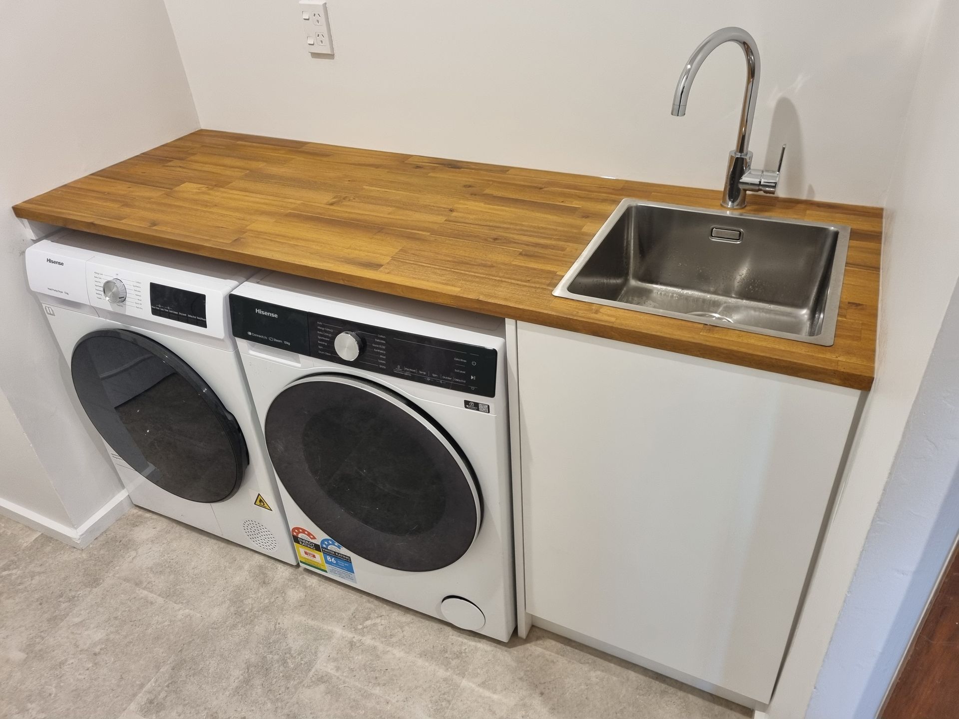 Renovated laundry with a timber benchtop above a side-by-side washer and dryer