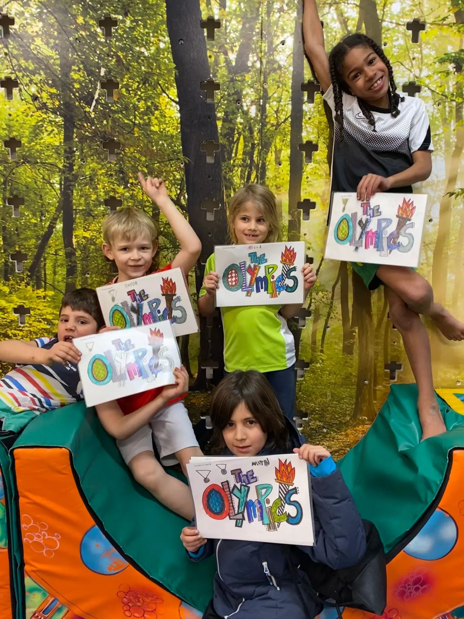 Five children hold up drawings with the word