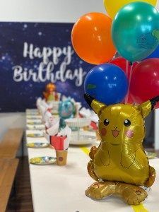 A Pikachu balloon stands at the end of a long party table set with plates, with a