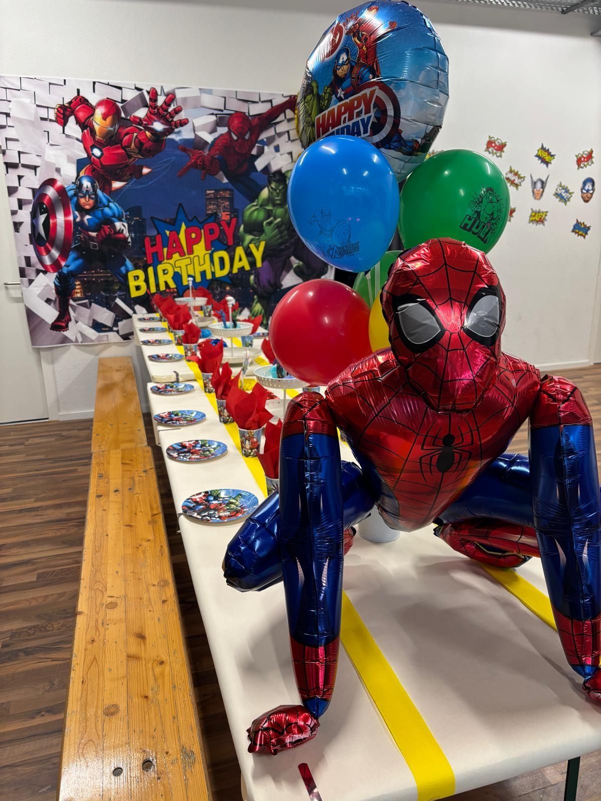 A long party table decorated with a Spider-Man theme, featuring a large Spider-Man balloon, balloons, and superhero decor.