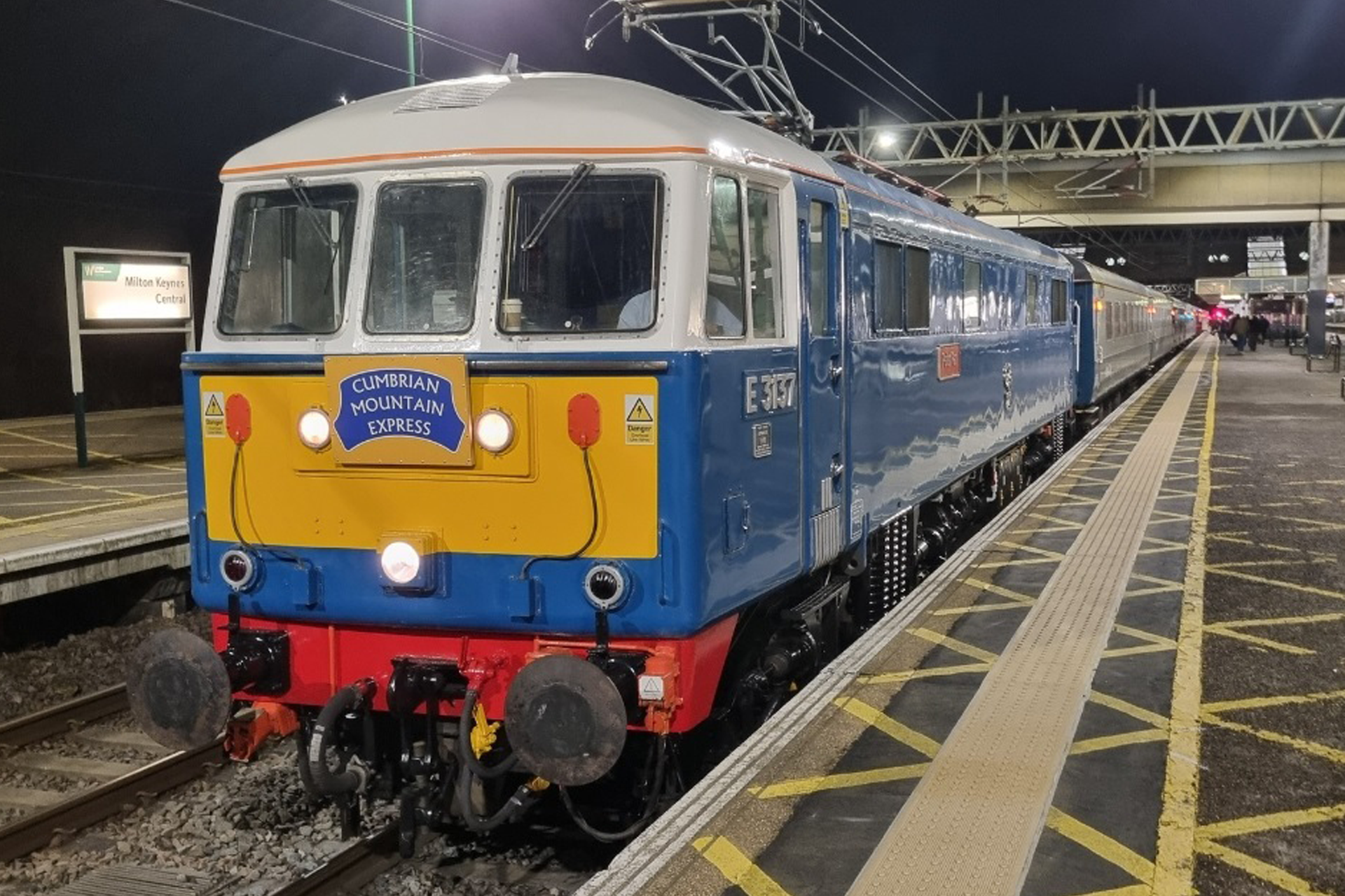 Blue and yellow electric train at a station platform at night