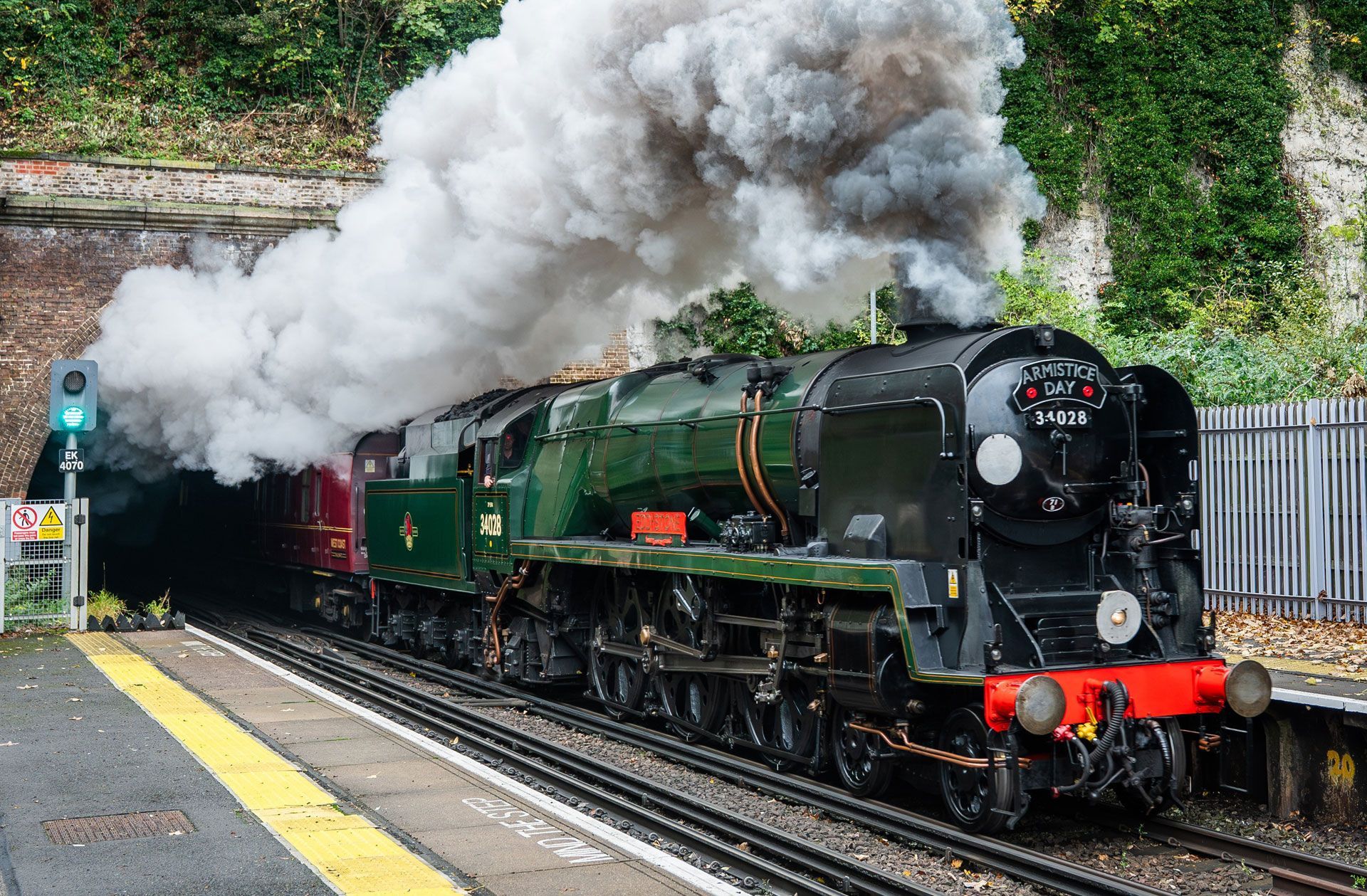 Steam locomotive with green carriages billowing smoke at a station platform