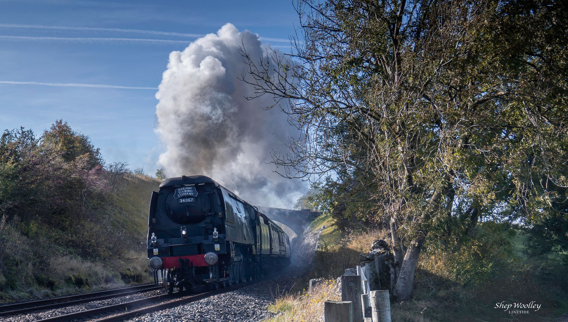 Steam train curving along coastal tracks, passing white buildings under a blue sky.