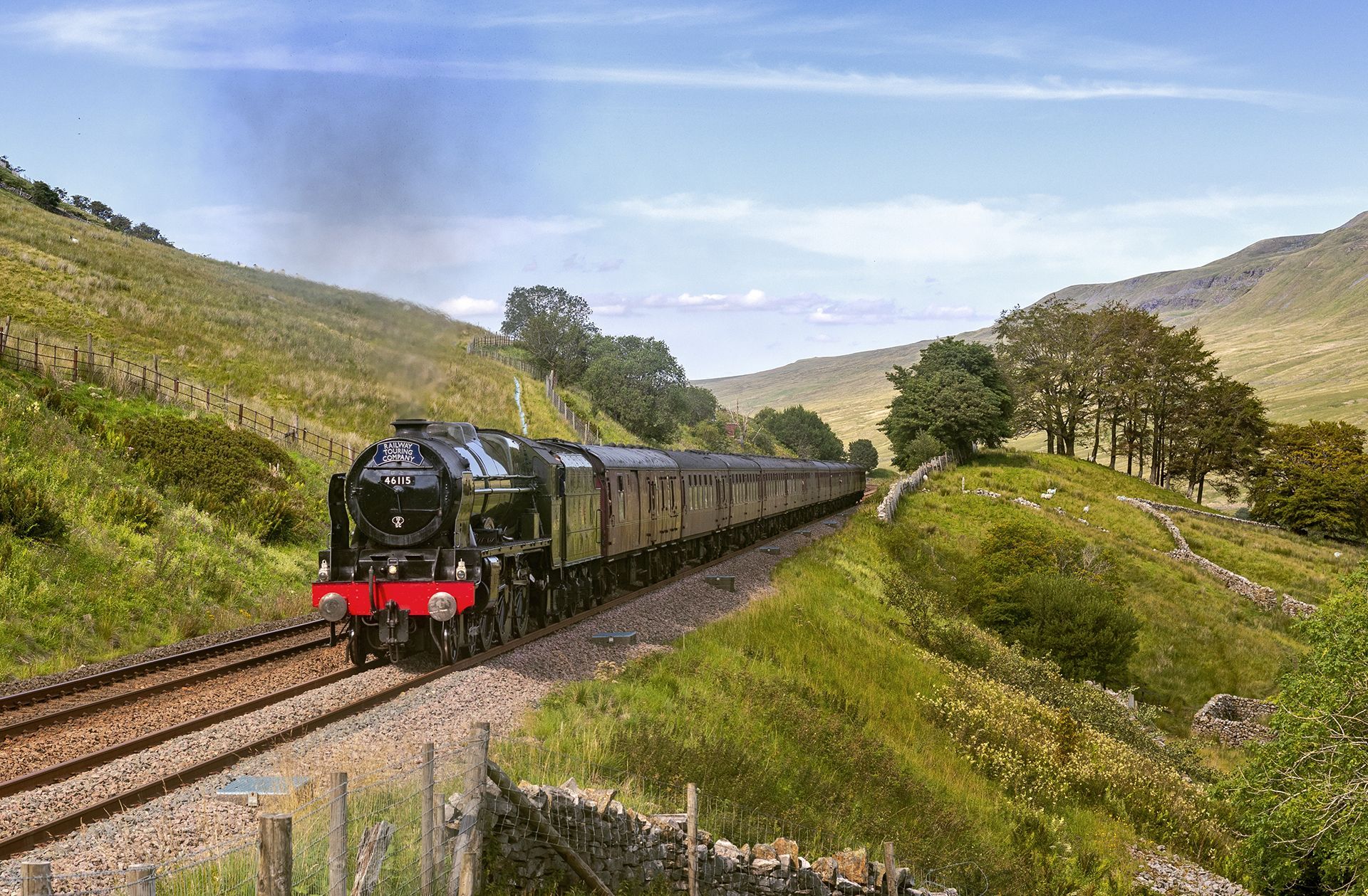 Black steam train crossing a green hillside valley under a blue sky