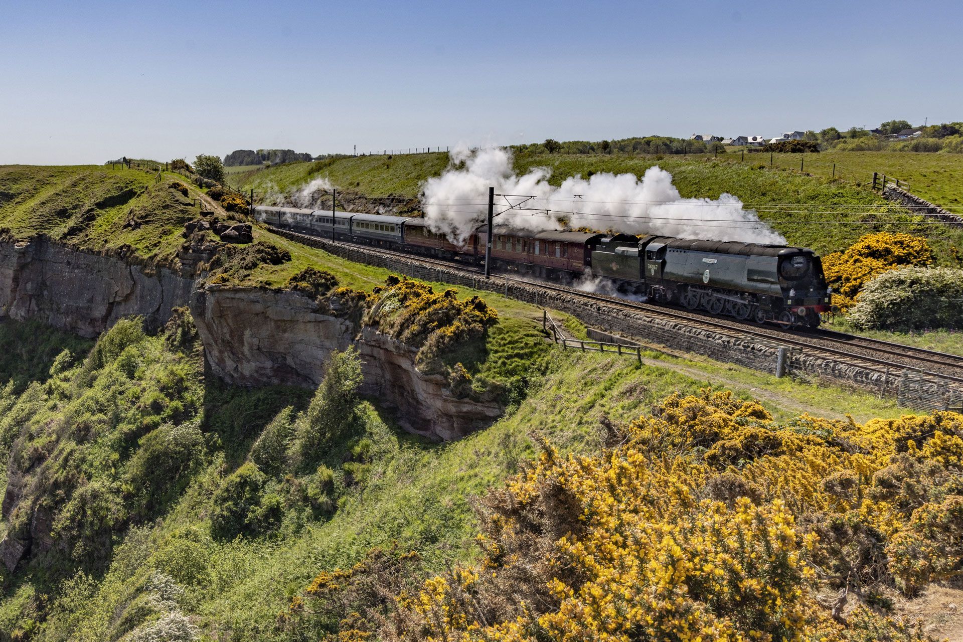 Steam locomotive crossing a cliffside viaduct through green countryside