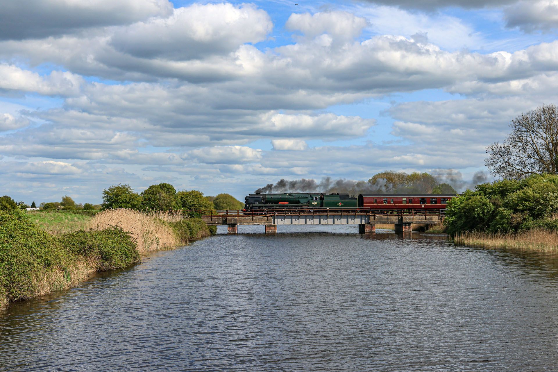 Wide river with a small bridge and a train crossing under a cloudy sky