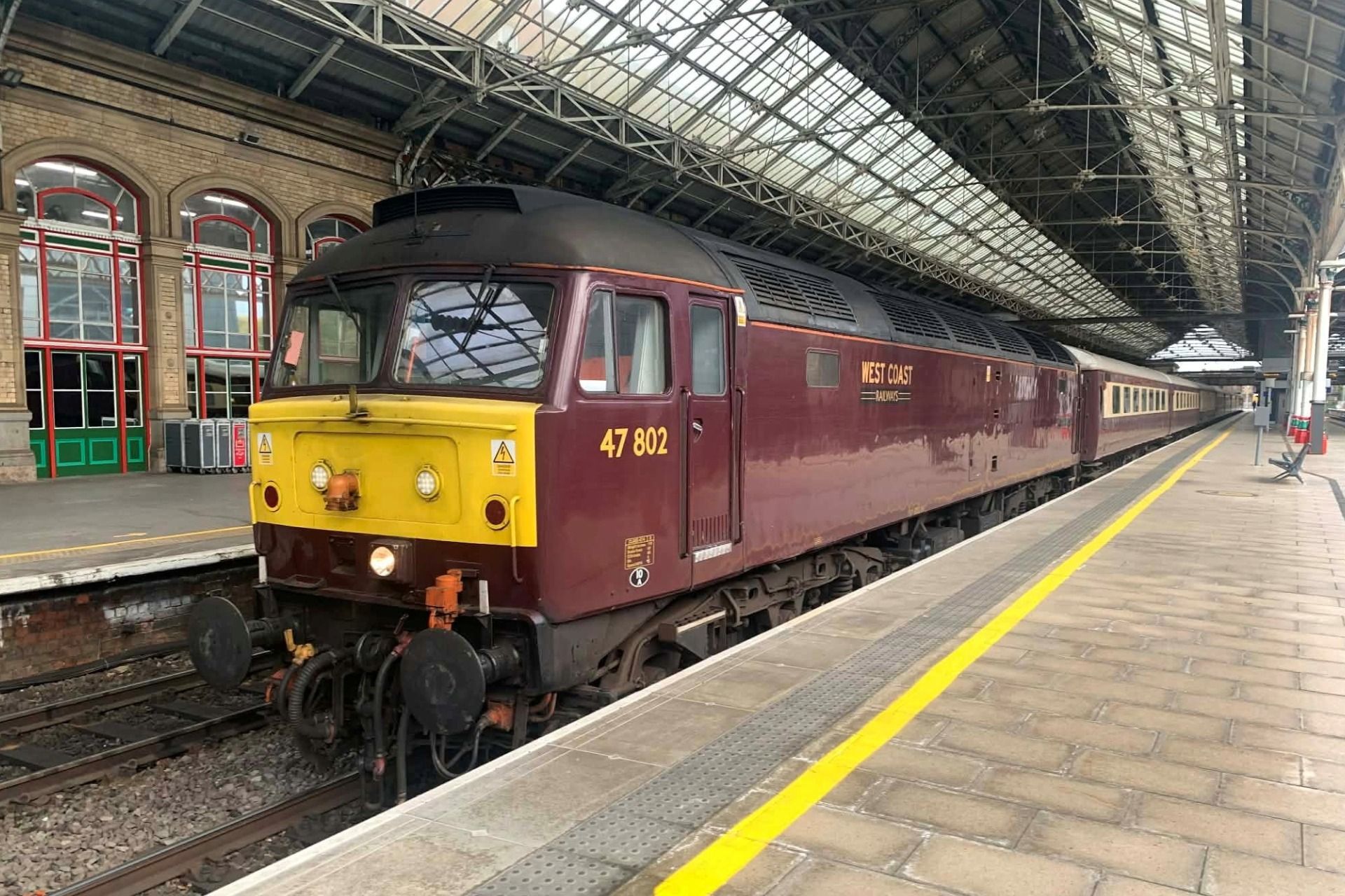 Maroon locomotive at a covered train station platform with yellow safety line