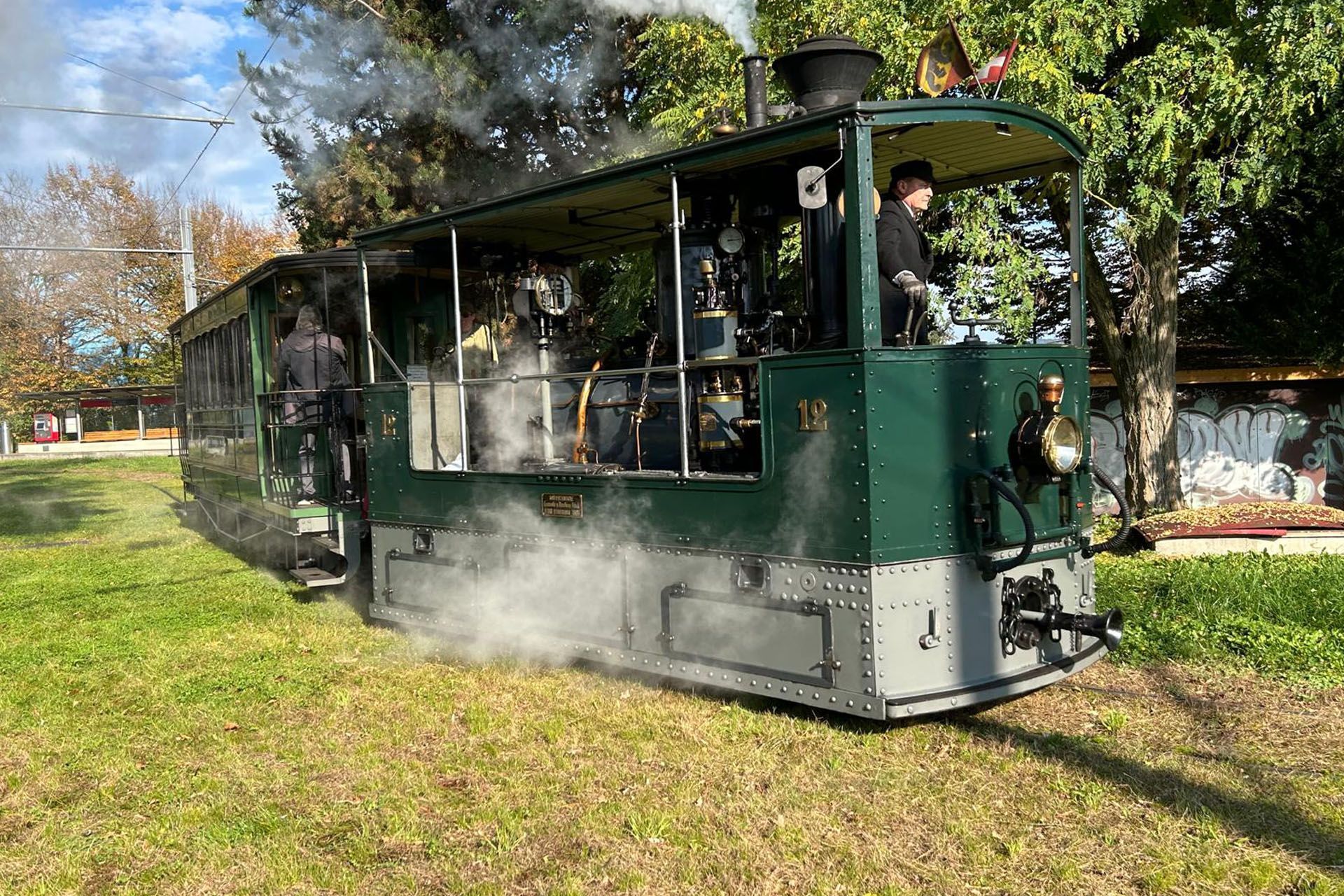 Green steam tram with passengers traveling through a park on a sunny day