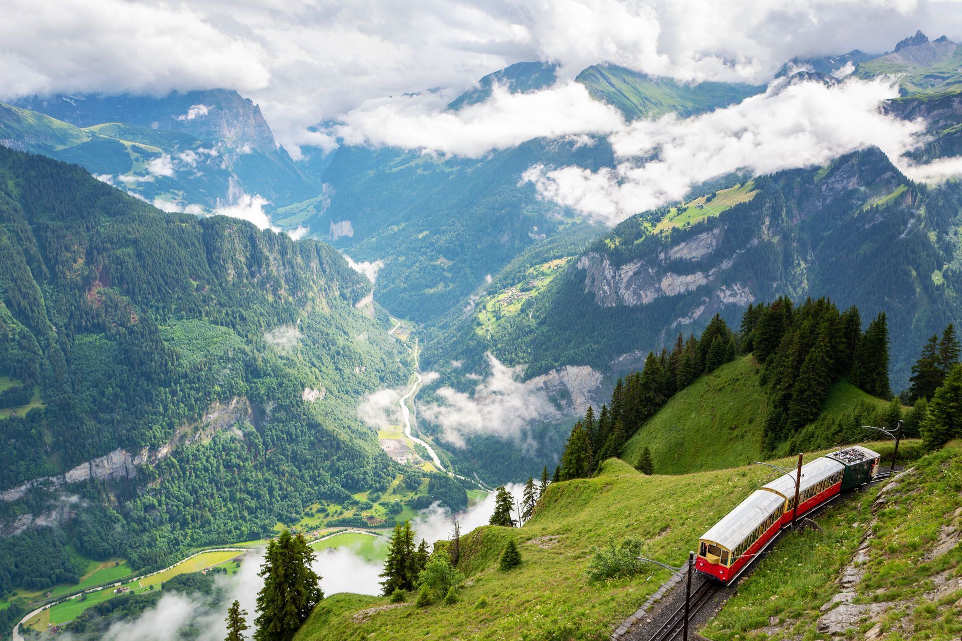 Mountain train winding through a lush alpine valley with misty peaks and green hills