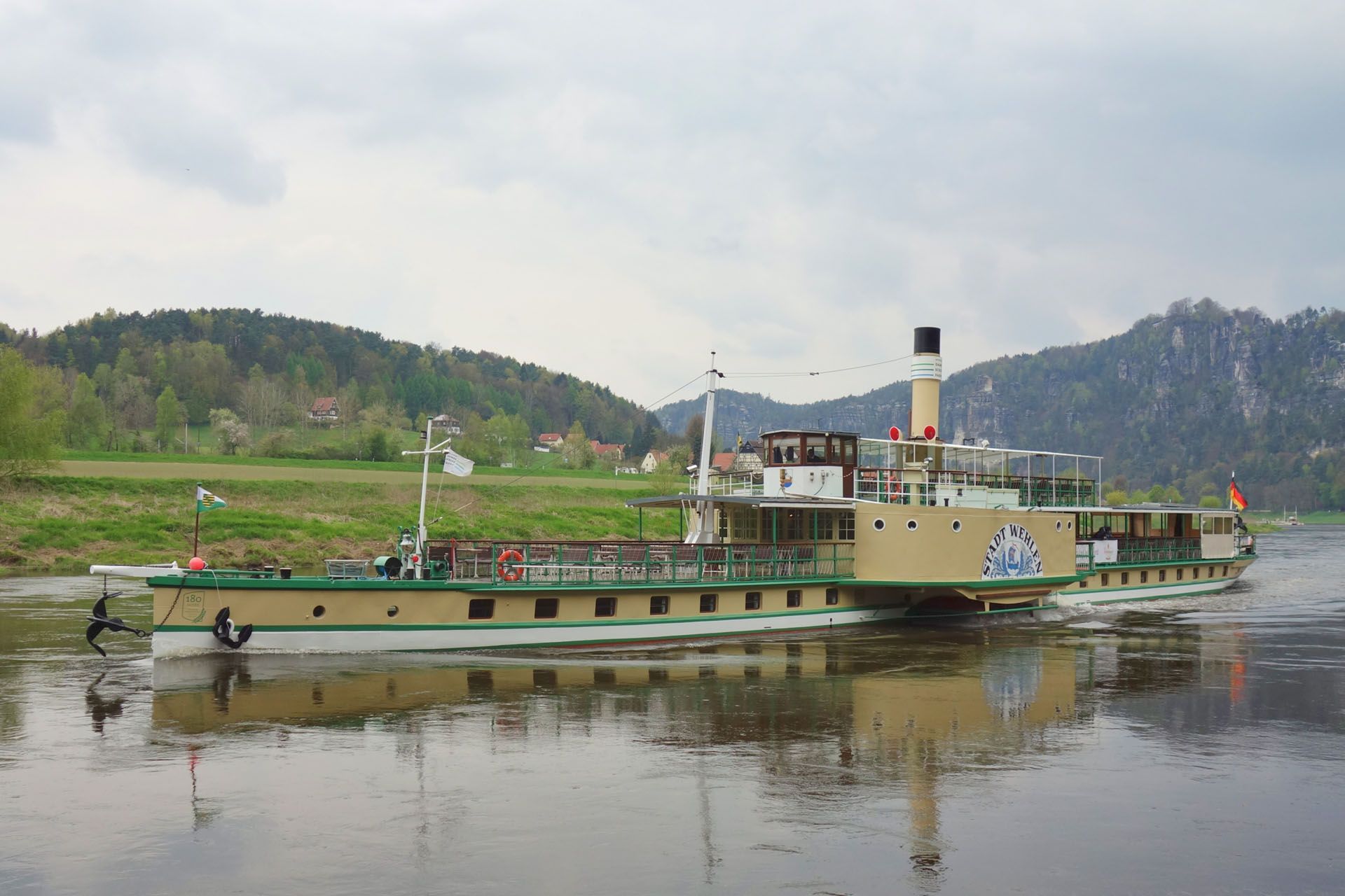 Long vintage riverboat on calm water with green hills and trees in the background