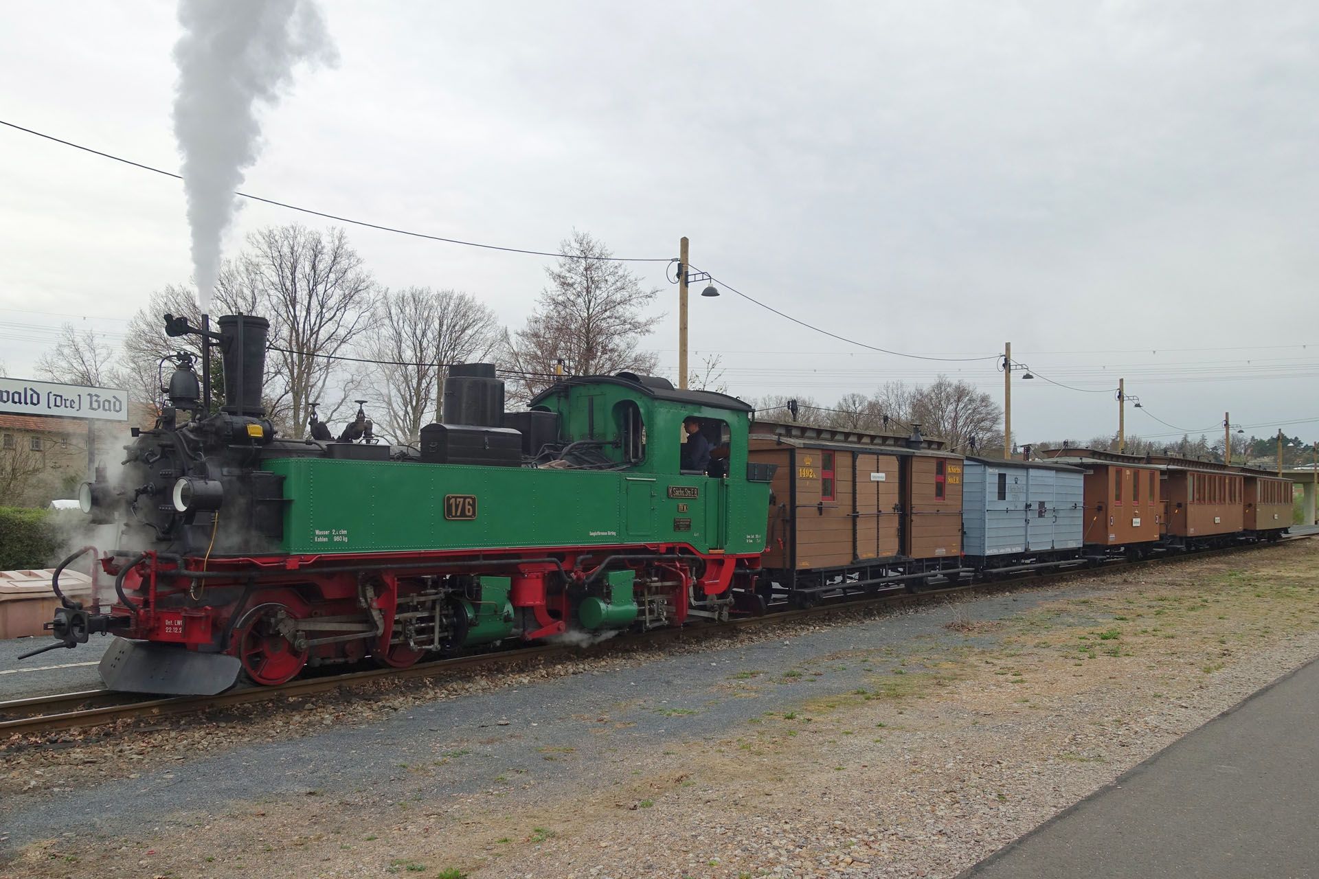 Green steam locomotive pulling freight cars on a track, with steam rising in an overcast outdoor setting
