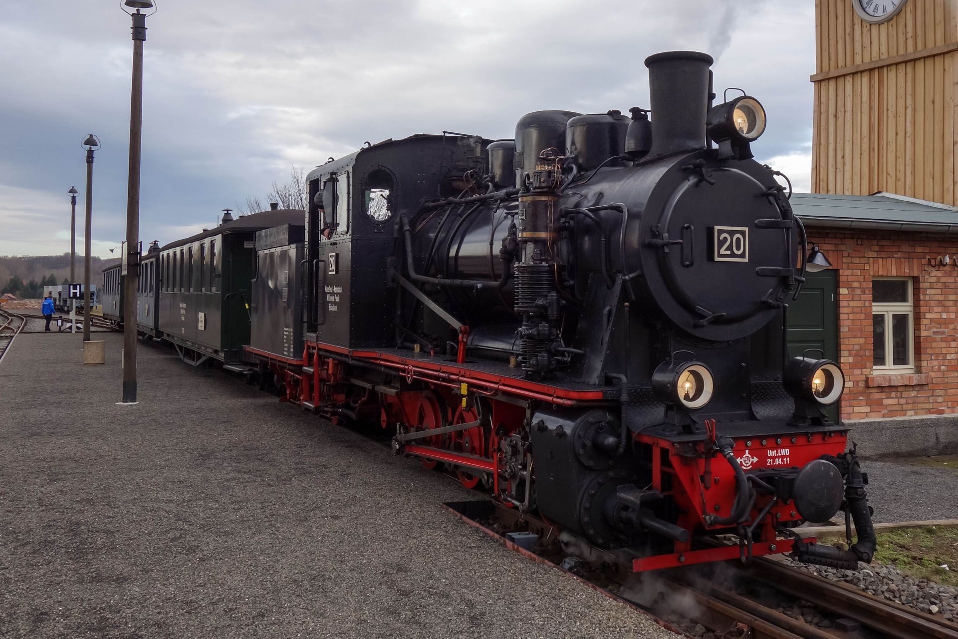 Black steam locomotive with red wheels pulling carriages on tracks at a station platform