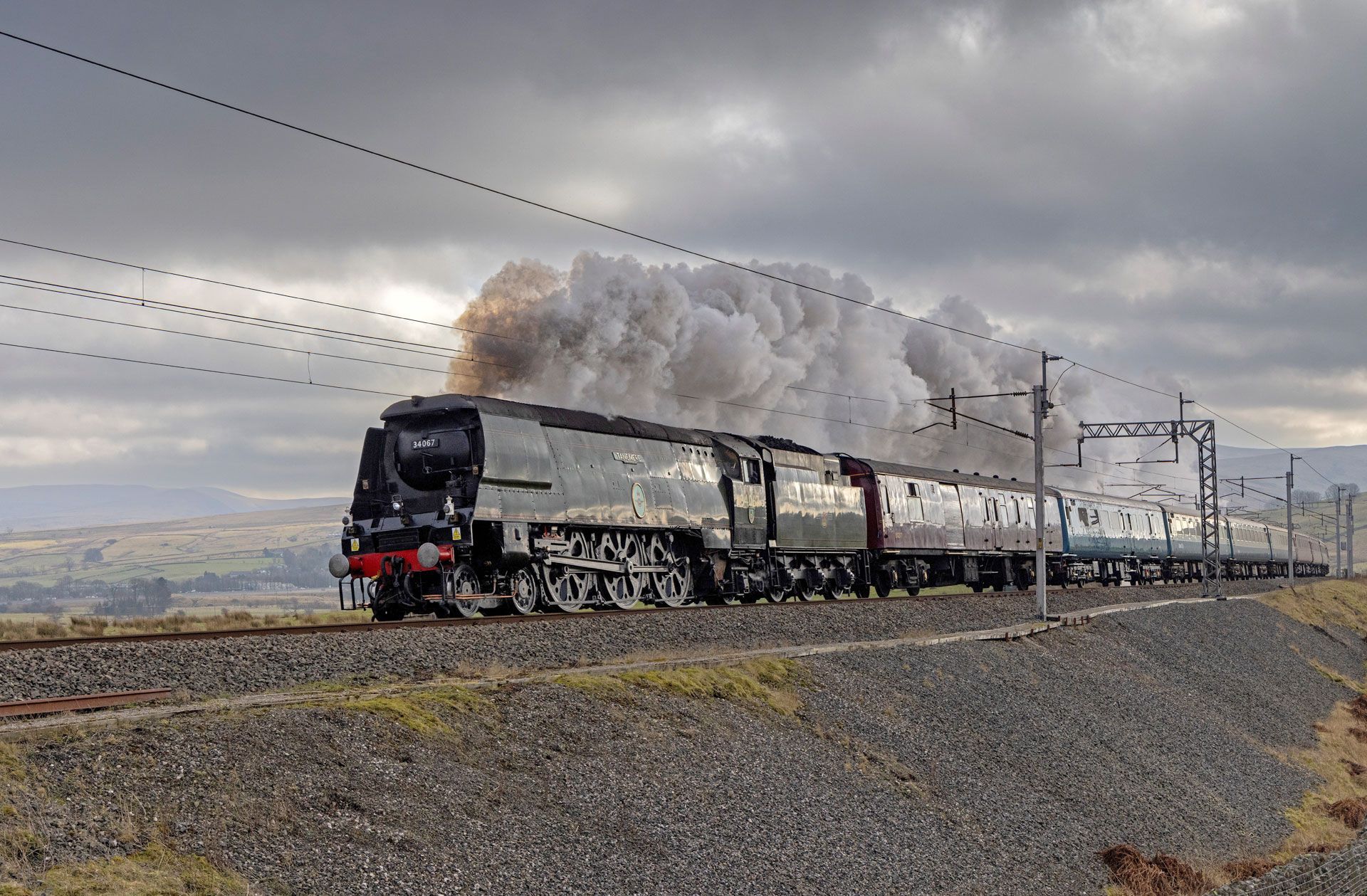 Steam locomotive pulling passenger cars across a cloudy rural landscape