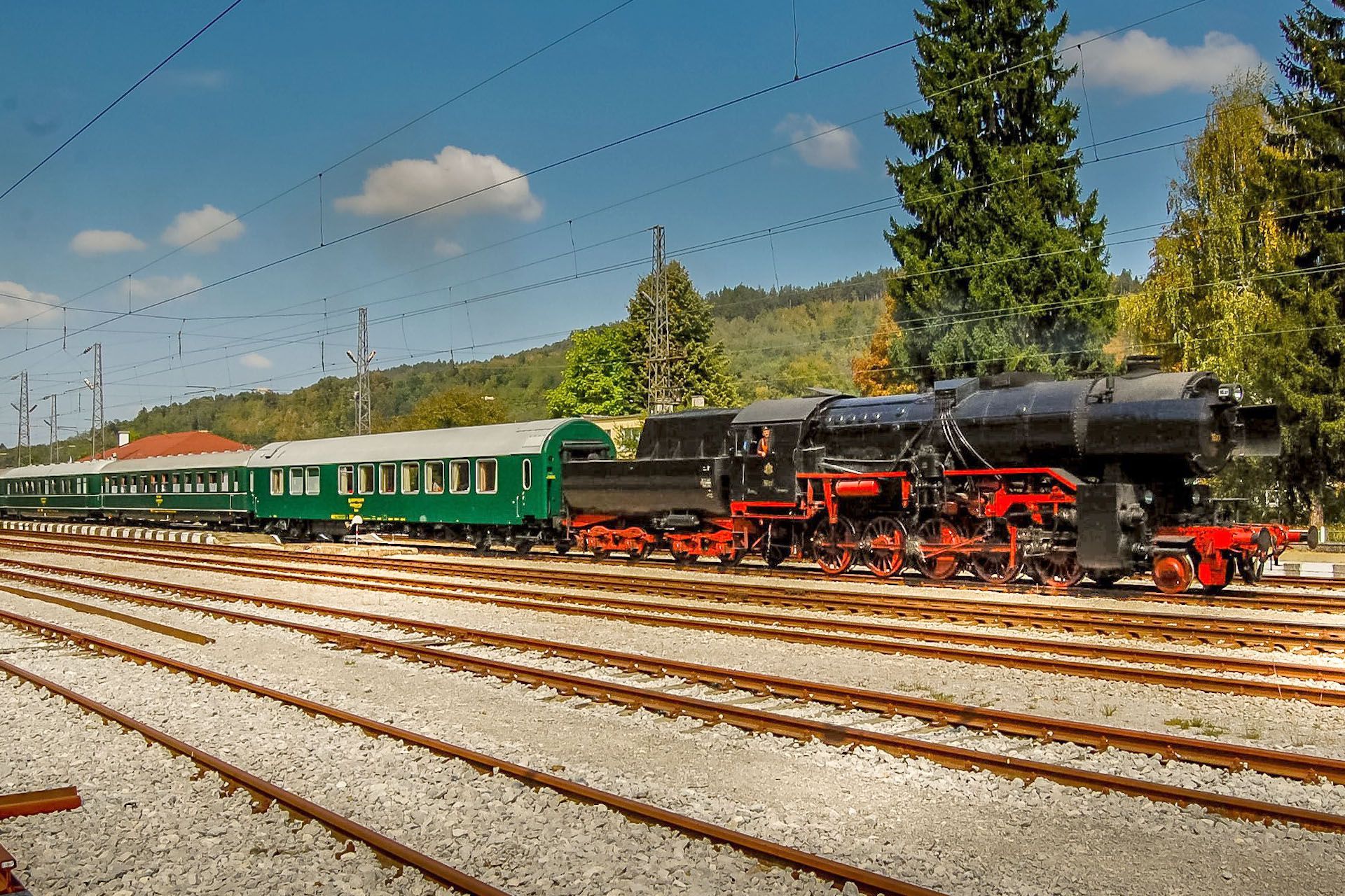 Steam locomotive with green passenger cars on railway tracks under a blue sky