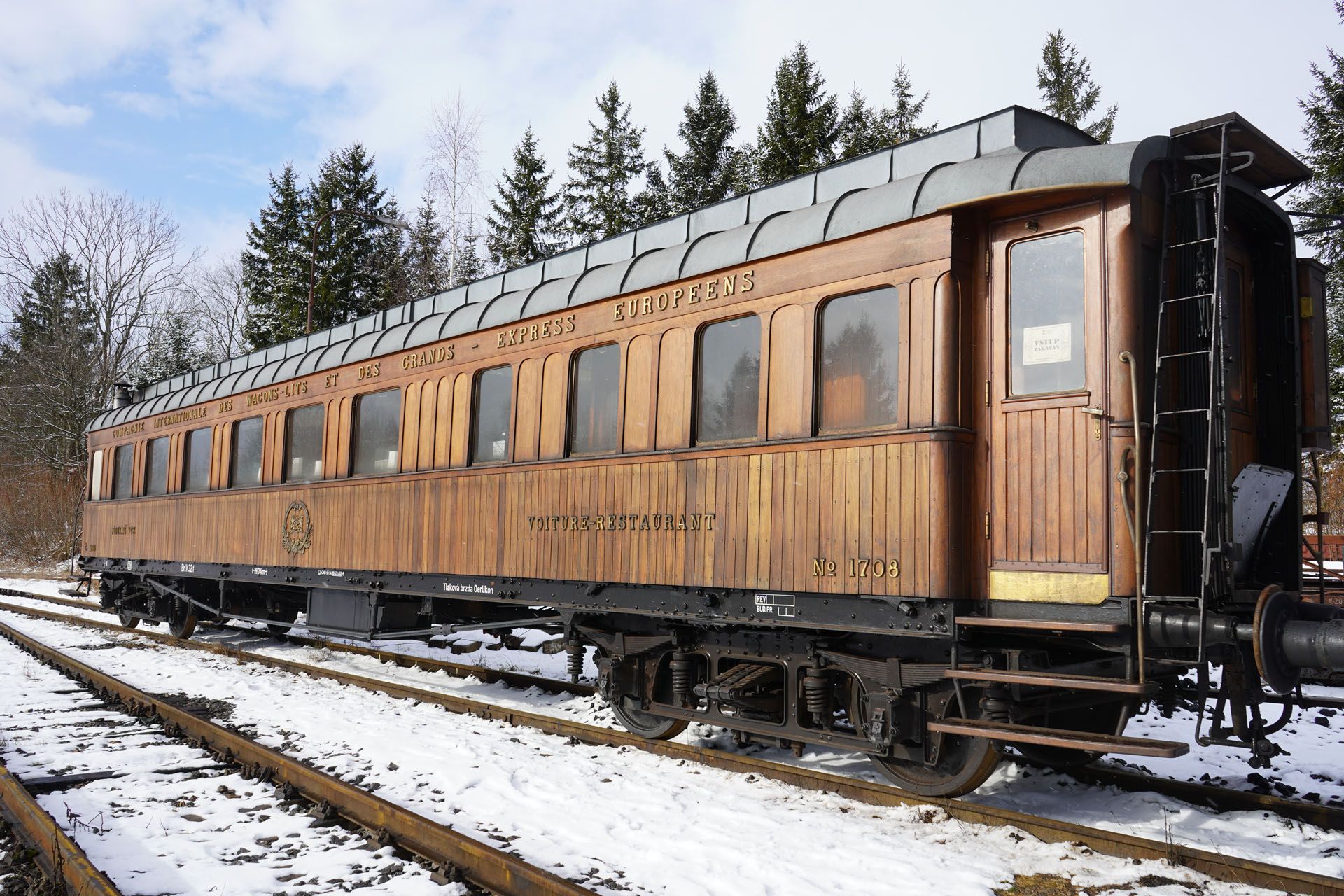 wooden vintage train cars on snowy tracks beside evergreen trees