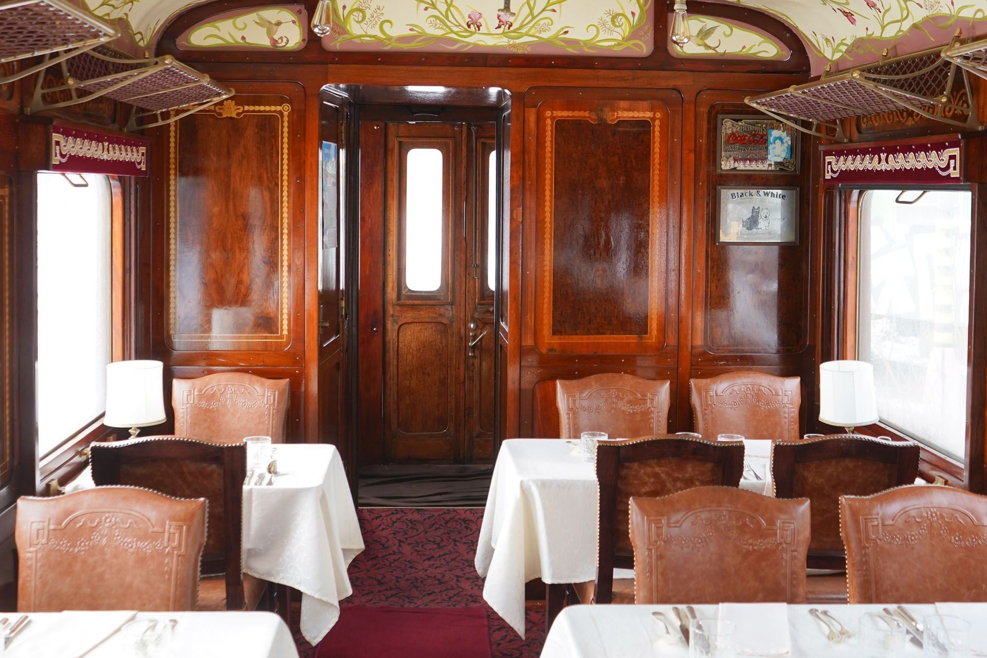 Elegant train dining car with polished wood paneling, white tablecloths, and upholstered seats