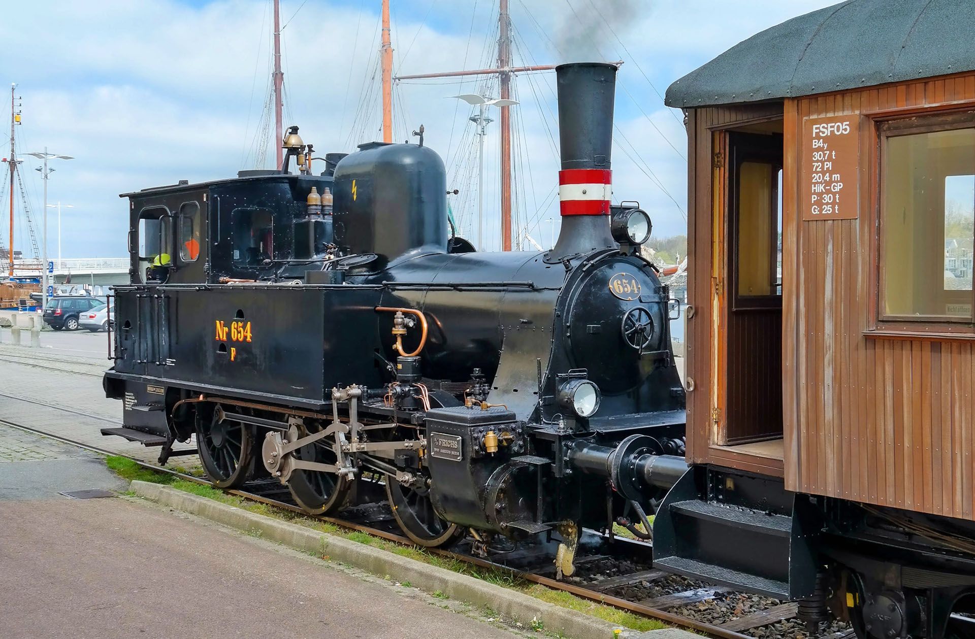 Black steam locomotive beside a wooden station platform, with red-and-white smokestack and snow on the ground