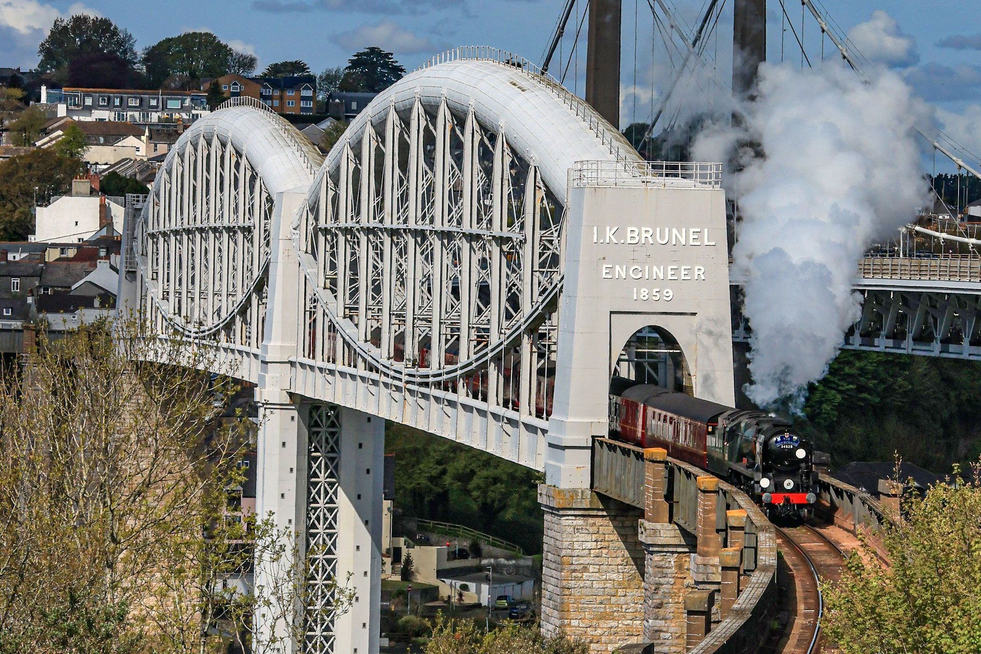 Steam train crossing a white arched bridge over a valley, with smoke rising in the background
