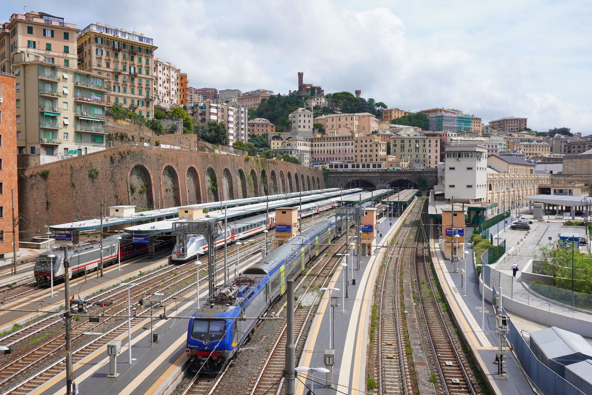 Railway station with multiple tracks and trains, surrounded by buildings on a hillside.