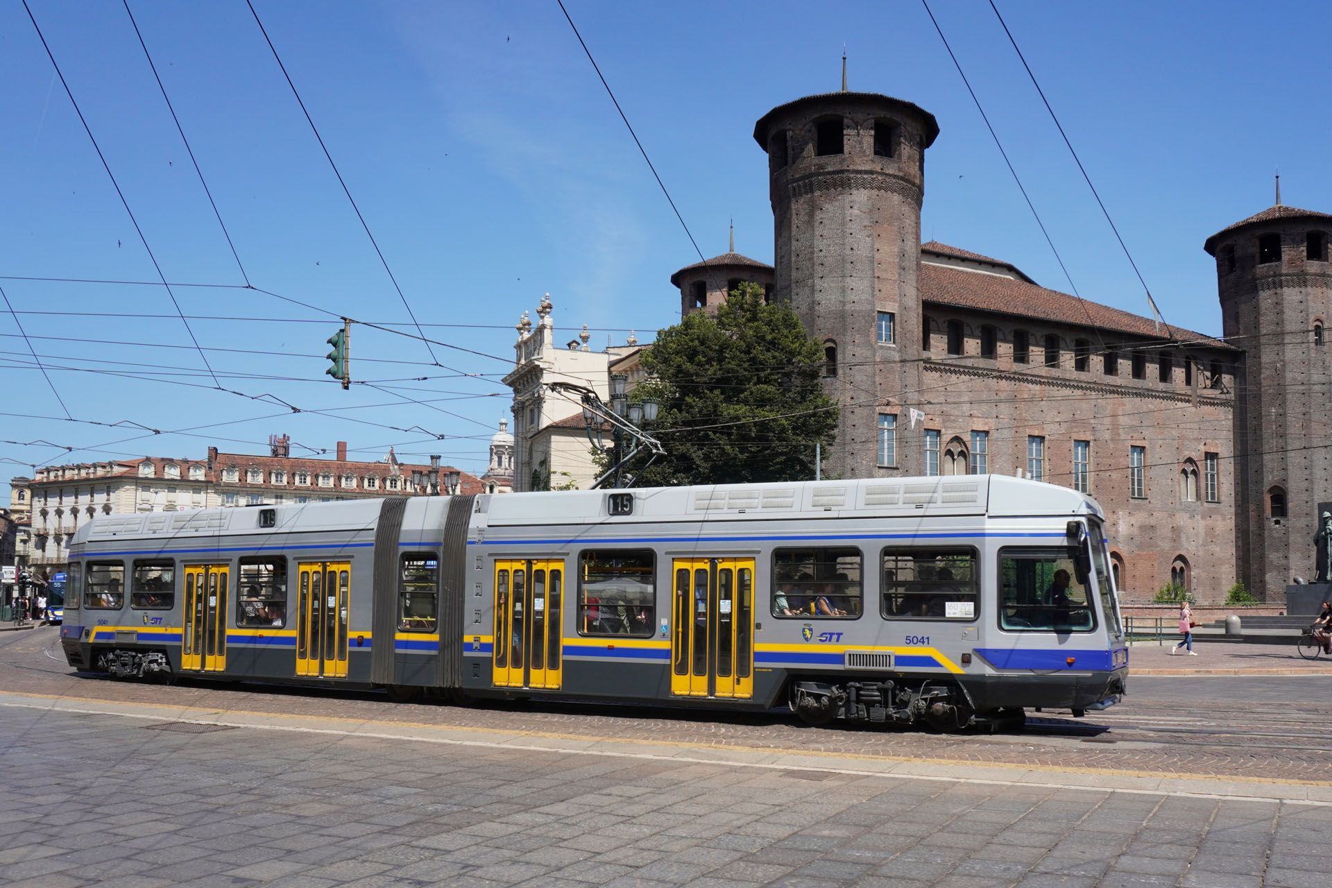 A light rail train in Turin, Italy, with a castle in the background on a sunny day.