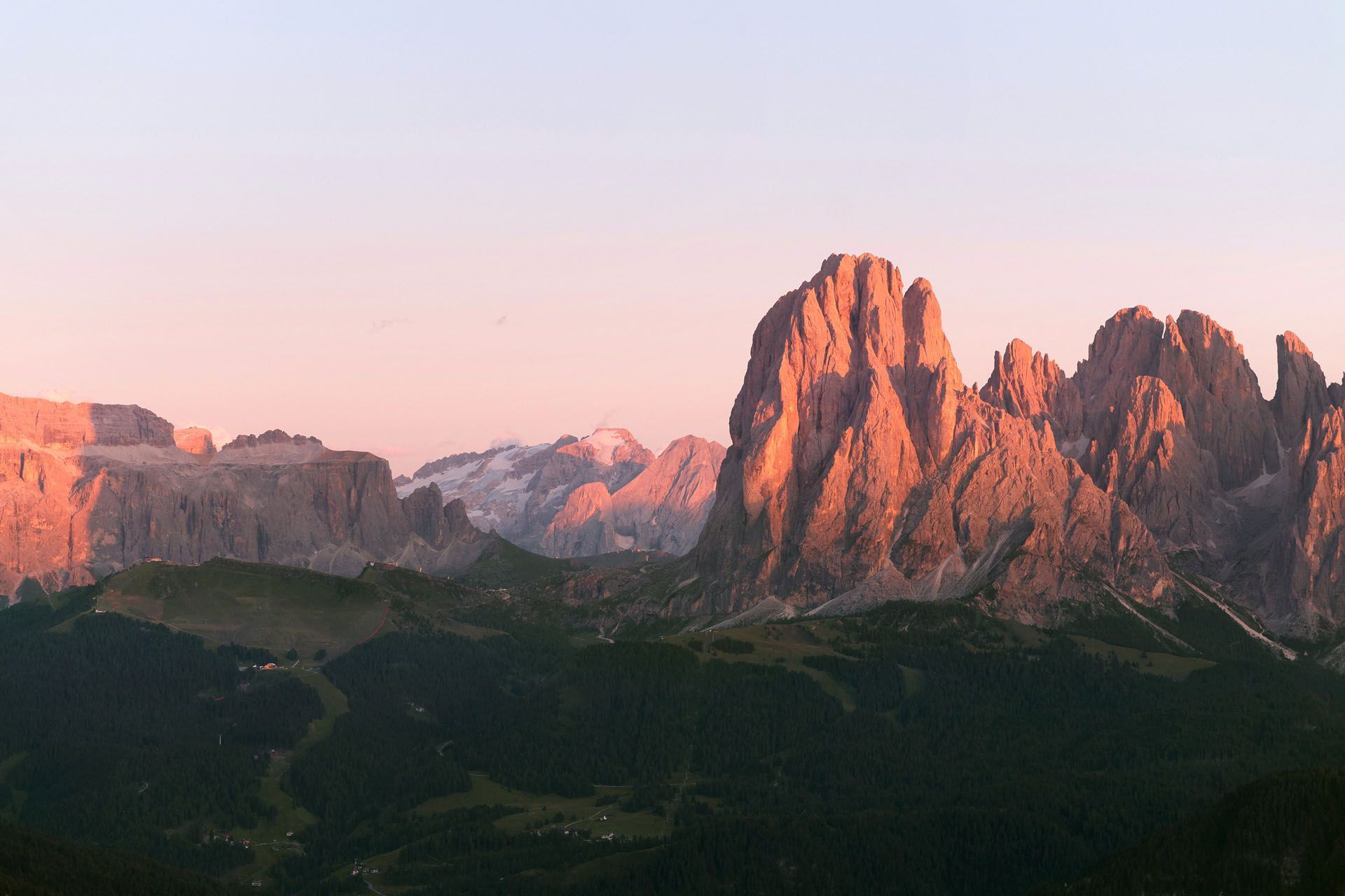 Sunset light on jagged pink mountain peaks above a dark green valley