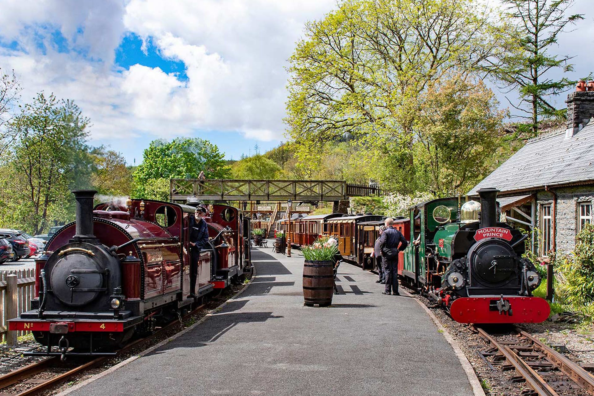 Two miniature steam trains on tracks at a sunny outdoor railway station