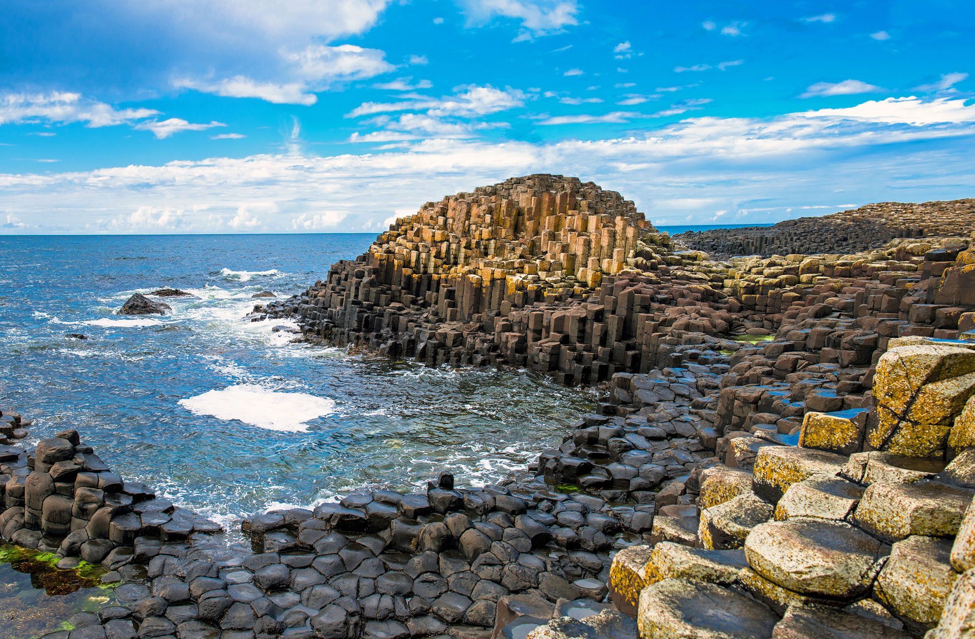 Basalt columns and rocky shoreline with ocean waves under a bright blue sky
