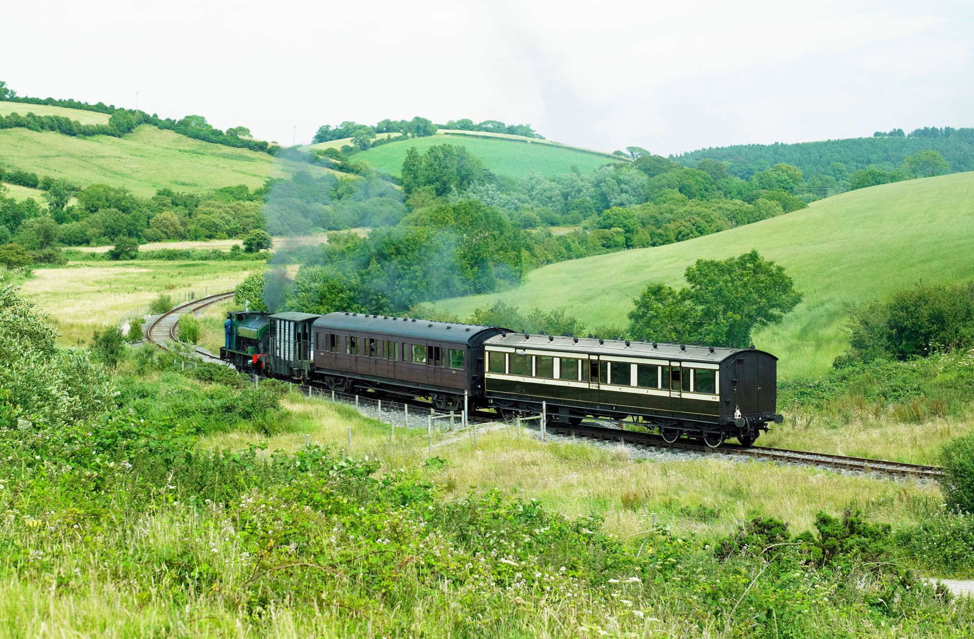 Steam train crossing green countryside hills under a bright sky