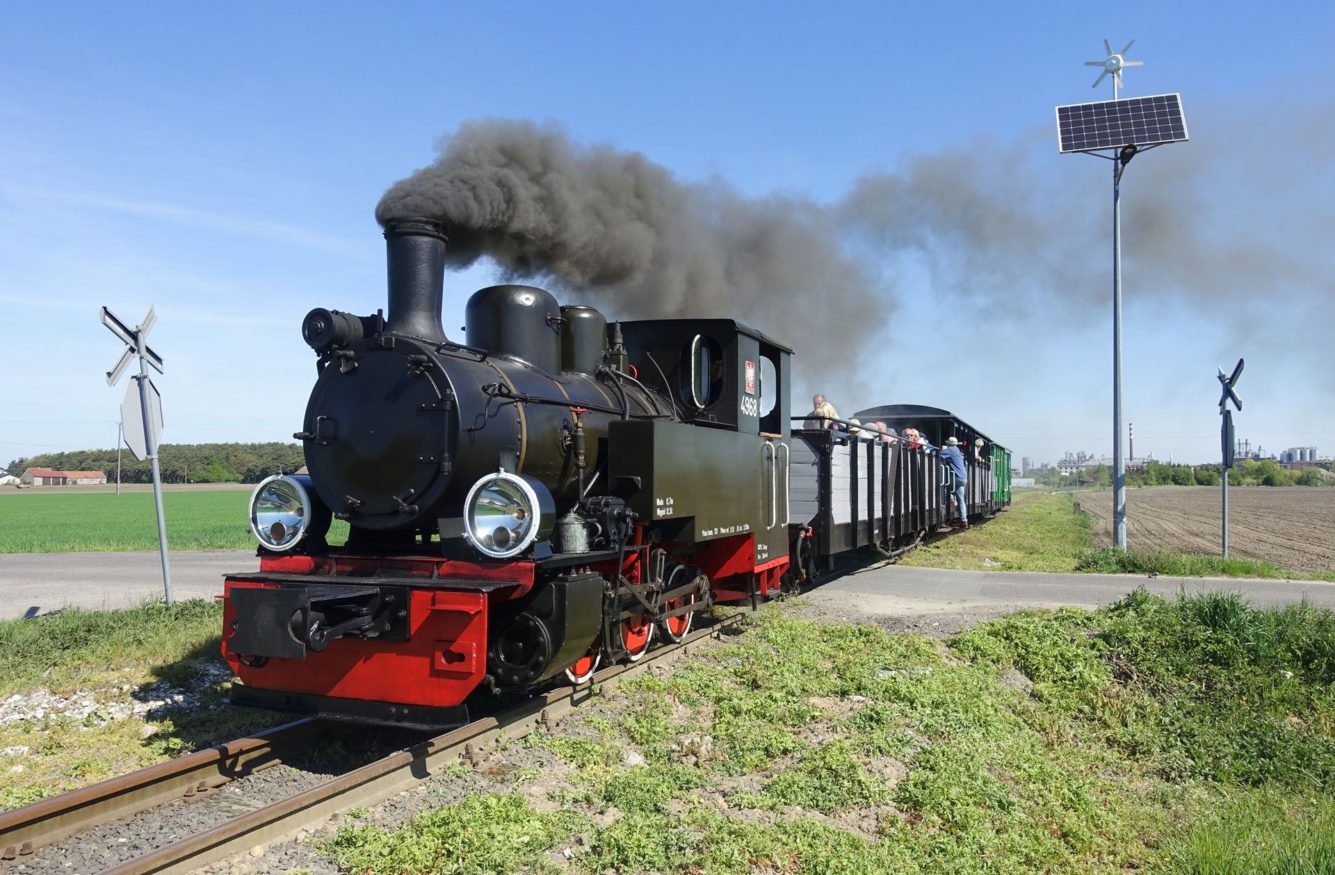 Black steam locomotive pulling passenger cars through a rural field, with smoke billowing from its stack