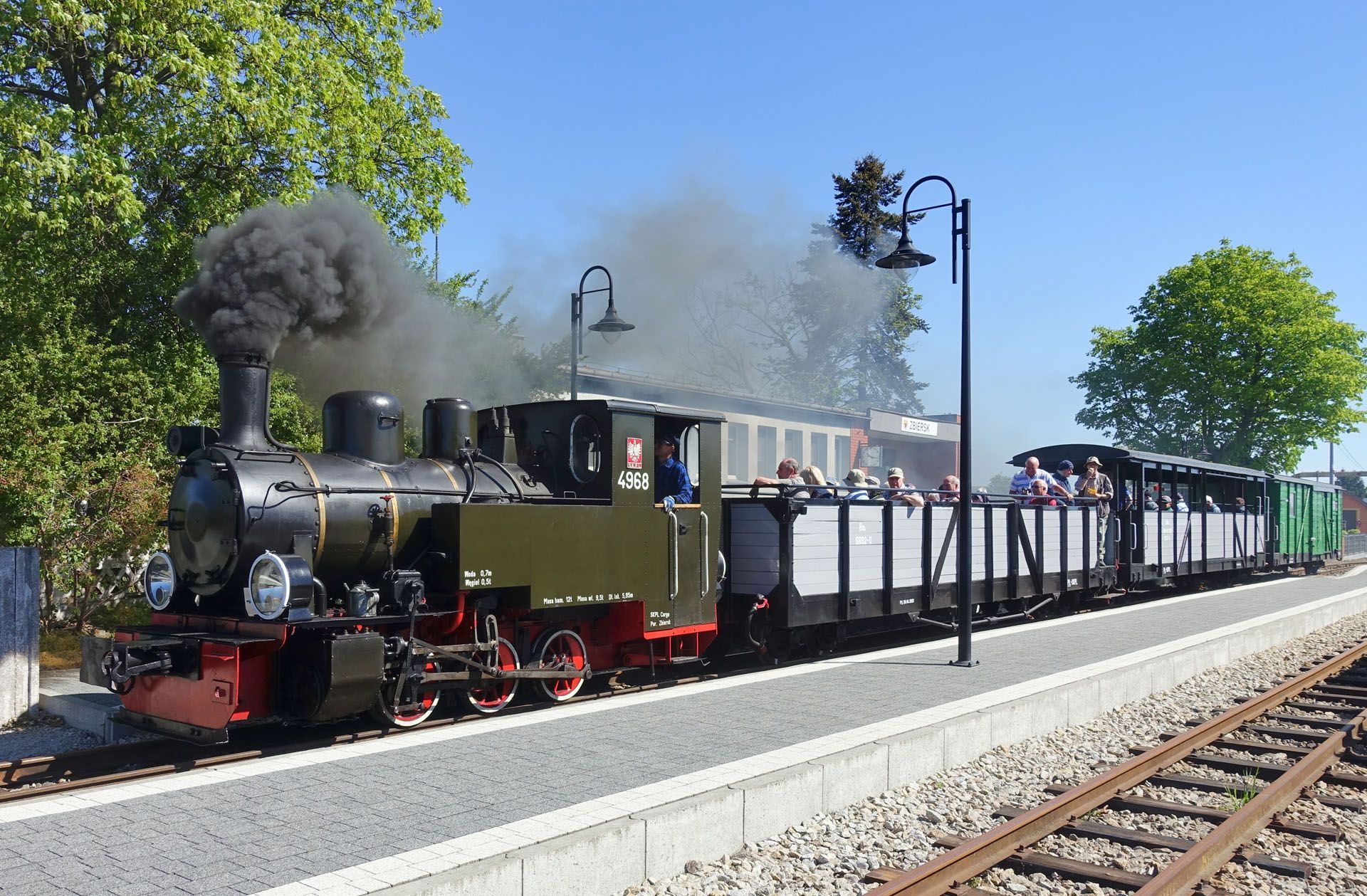 Steam locomotive pulling a long freight train past a platform on a sunny day