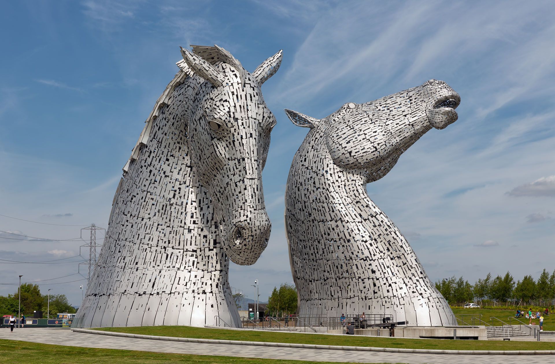 Two giant silver horse-head sculptures in a grassy field under a blue sky